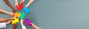 team of people, hands in holding puzzle pieces that fit together